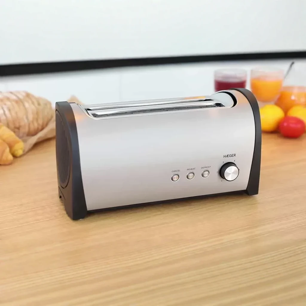 Tostadora Haeger Desayuno Plus 6 1400W 2 Ranuras Negro, en uso: sobre encimera de madera con pan y zumos al fondo, vista