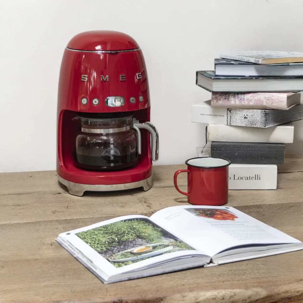 Cafetera de goteo Smeg 1,4L 1050W Rojo DCF02RDEU, en uso: sobre mesa de madera con jarra llena, taza roja y libros apilados