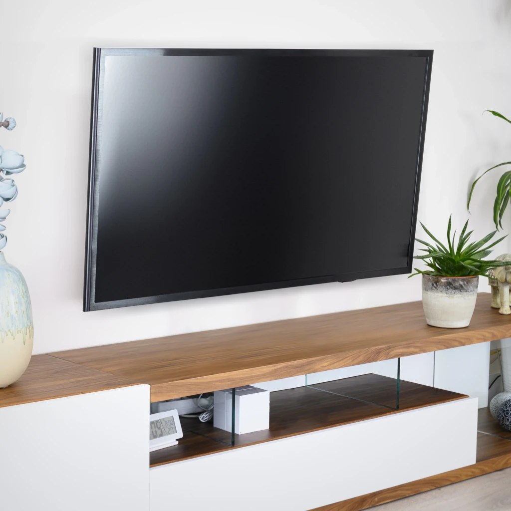 Soporte TV TooQ Negro Pared Inclinable 32-55 pulgadas LP4255T-B, en uso: TV montada en pared blanca sobre mueble de madera