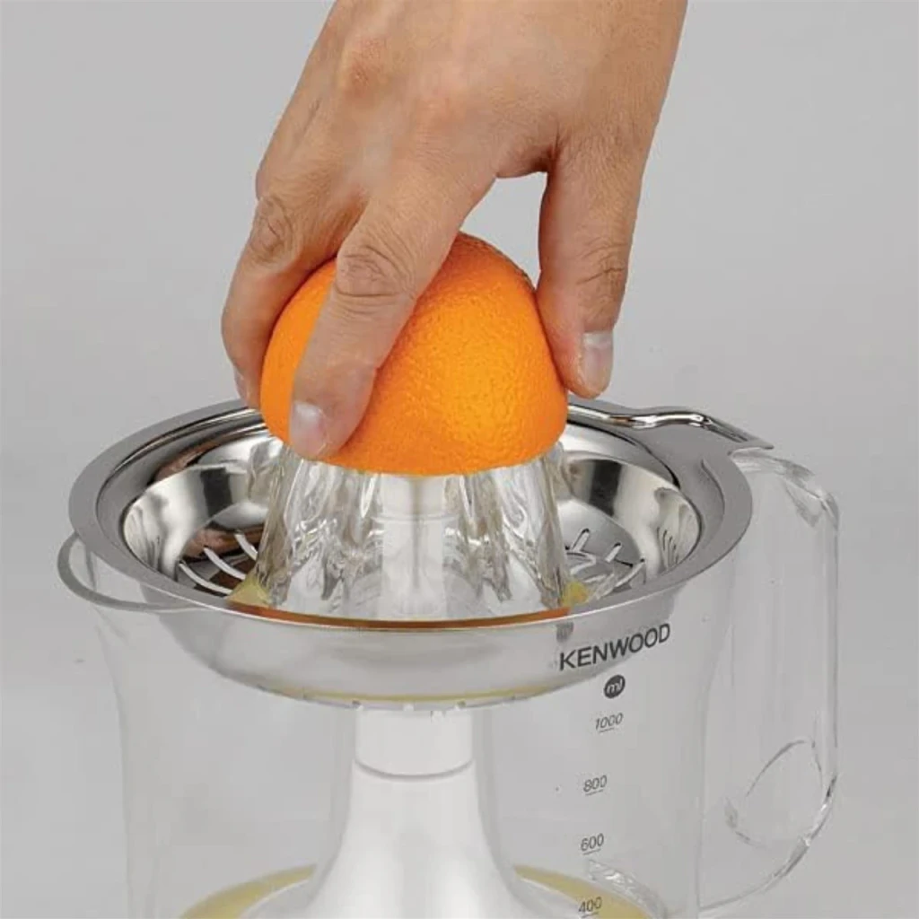 Exprimidor Kenwood JE290 1L 40W Blanco, en uso: mano presionando naranja sobre cono inox, jarra con zumo visible