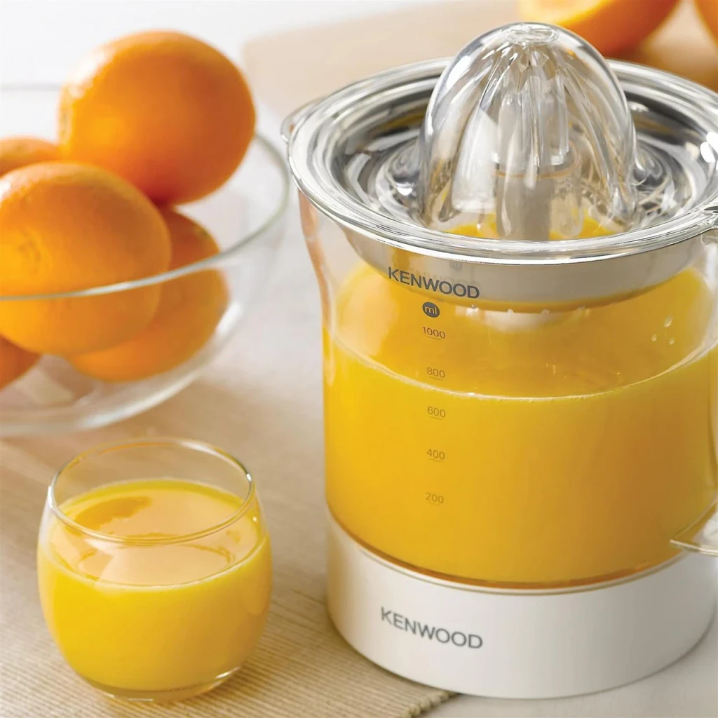 Exprimidor Kenwood JE290 1L 40W Blanco, en uso: jarra llena de zumo de naranja, vaso servido y naranjas al fondo