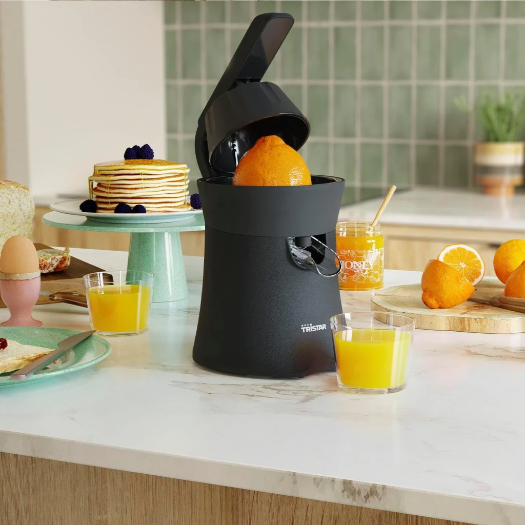 Exprimidor Tristar 120W Negro CP-3015, en uso: tapa abierta con naranja dentro, vasos de zumo y desayuno en cocina