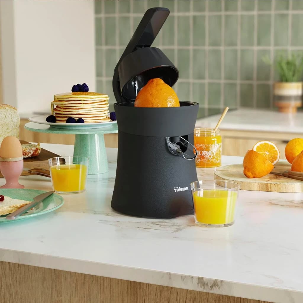Exprimidor Tristar 120W Negro CP-3015, en uso: tapa abierta con naranja dentro, vasos de zumo y desayuno en cocina