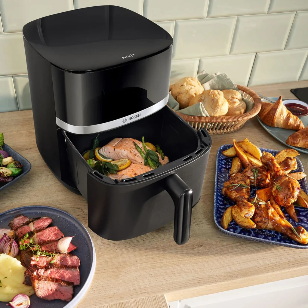 Freidora de aire Bosch Serie 4 6,1L 2050W Negro MAF462B0, en uso: cesta abierta con salmón, rodeada de platos cocinados