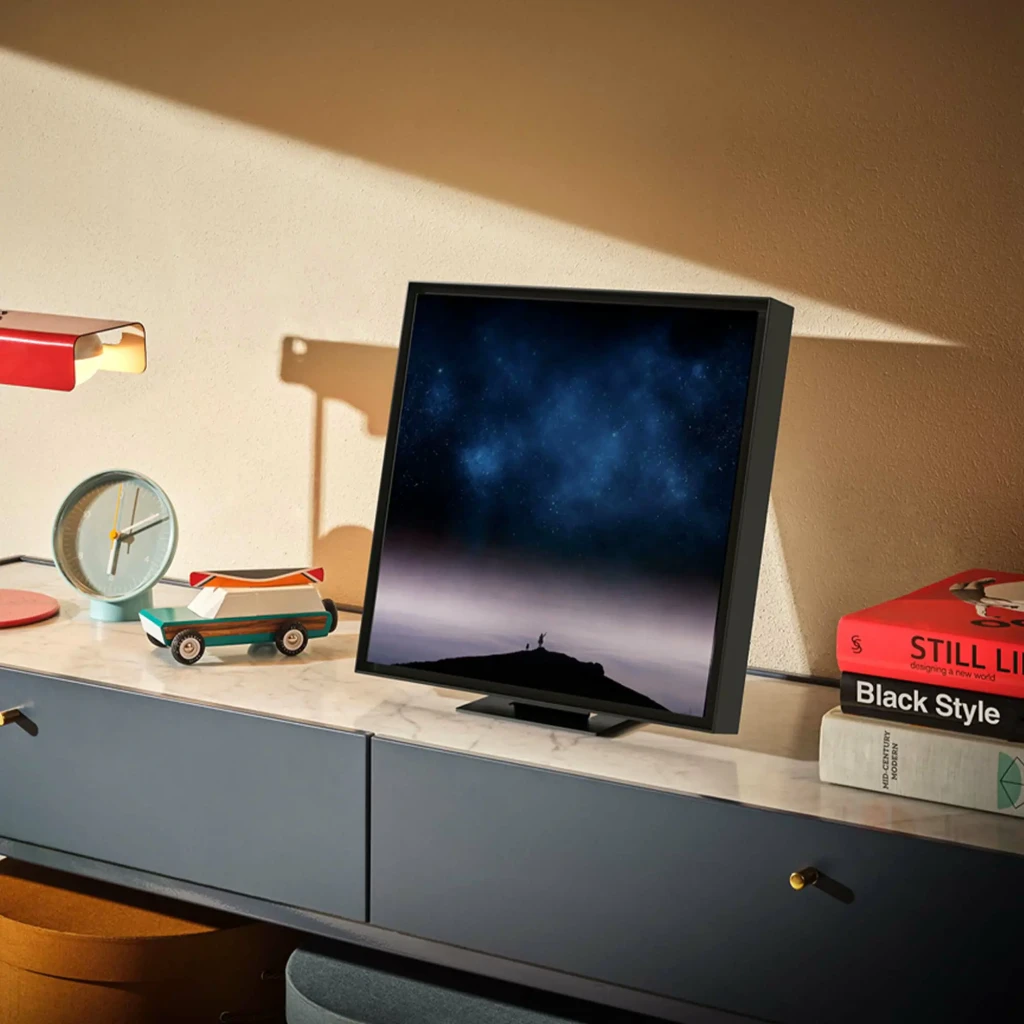 Altavoz Samsung Music Frame Dolby Atmos 2.0 Bluetooth 5.2 Negro HW-LS60D, en uso: sobre cómoda con reloj y libros, mostrando