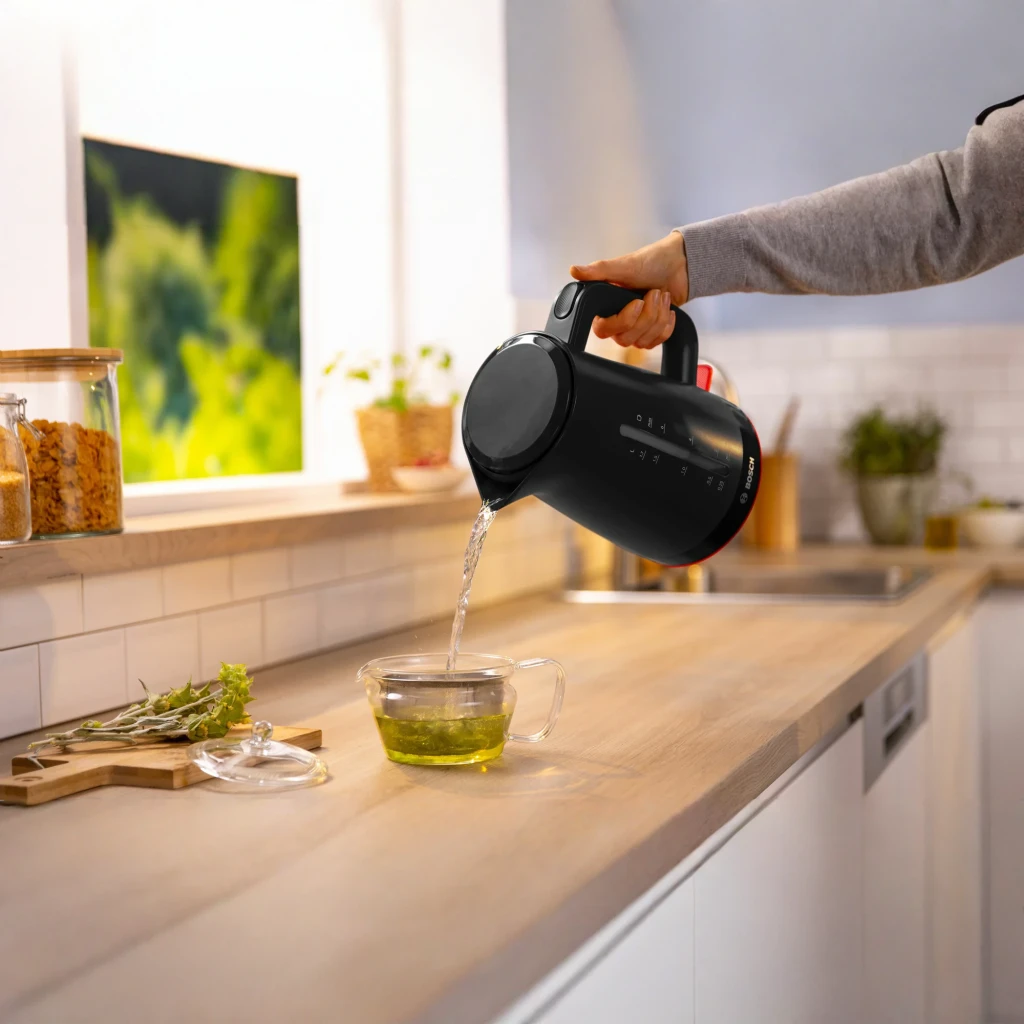 Chaleira elétrica Bosch MyMoment 1,7L 2400W Preto TWK3M123, em uso: mão a verter água em chávena de chá sobre bancada