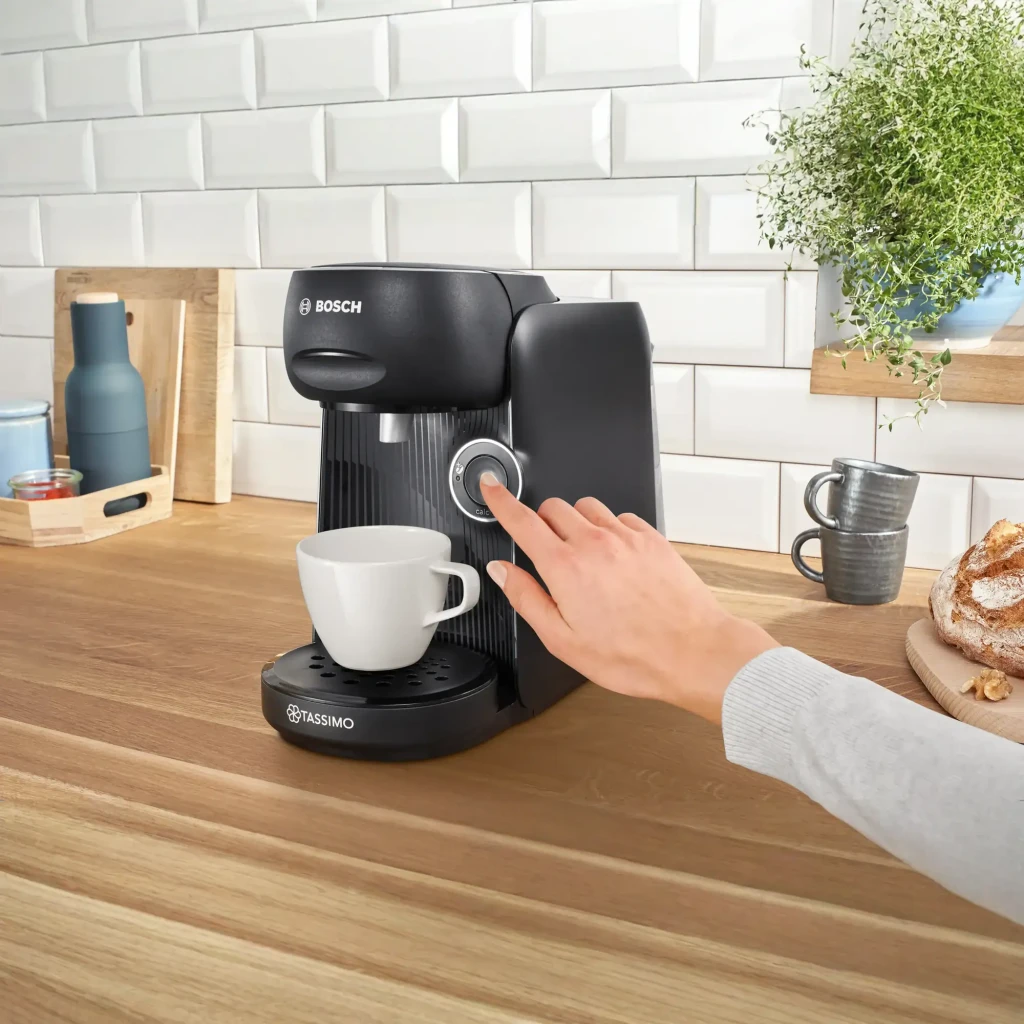 Máquina de café em cápsulas Bosch Tassimo Finesse 0,7L T DISC 1400W Preto TAS162E, em uso: mão a pressionar o botão