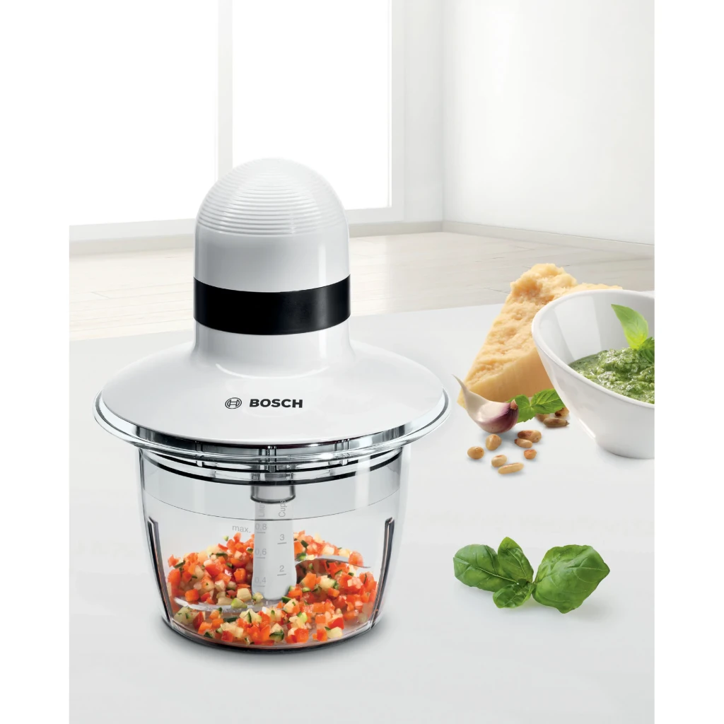 Hachoir Bosch 0,8L 400W Blanc MMR08A1, en utilisation: bol transparent avec légumes hachés, pesto et parmesan en arrière-plan