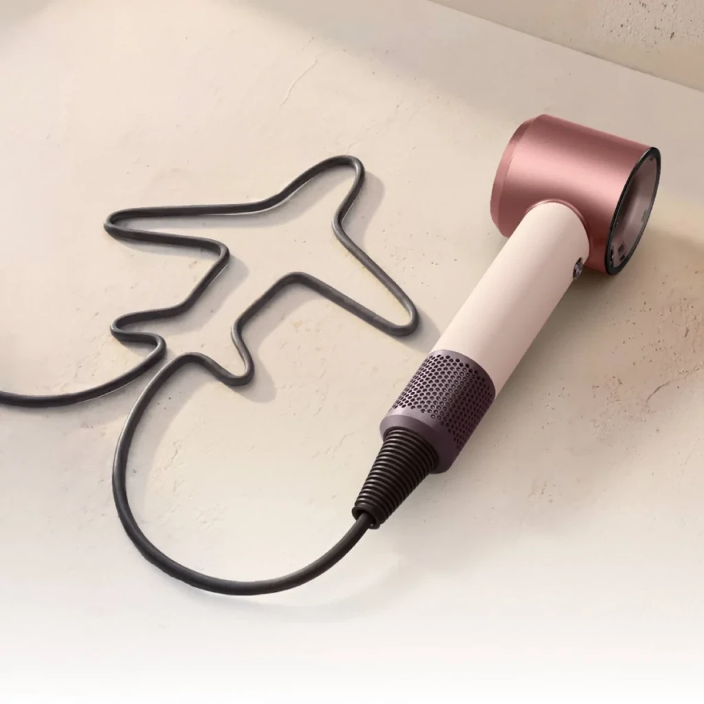 Secador de pelo Dyson Supersonic Travel 1220W Rosa, en uso: sobre superficie con cable formando silueta de avión