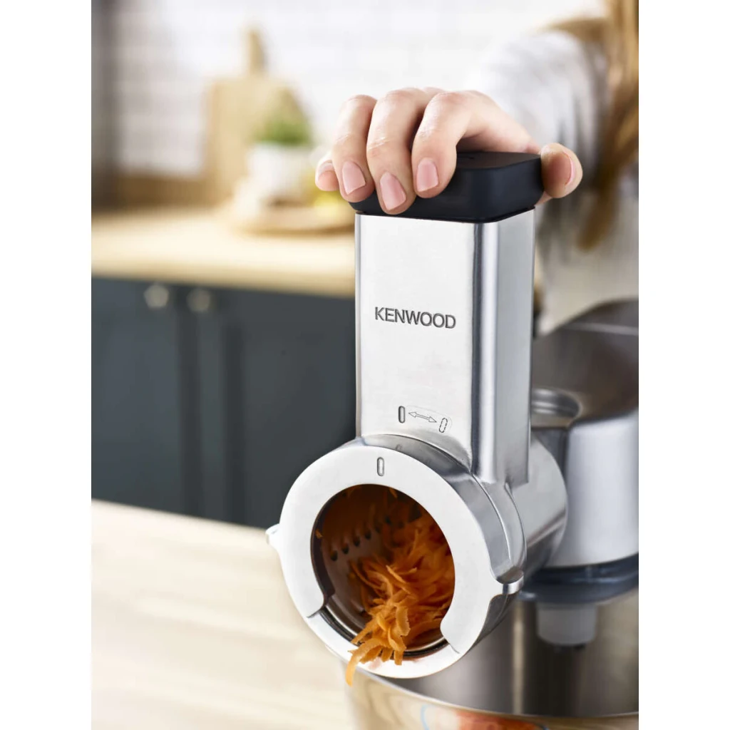 Découpeur Rotatif Kenwood KAX643 Argent, en cours d'utilisation: main poussant l'aliment, carotte râpée tombant dans le bol