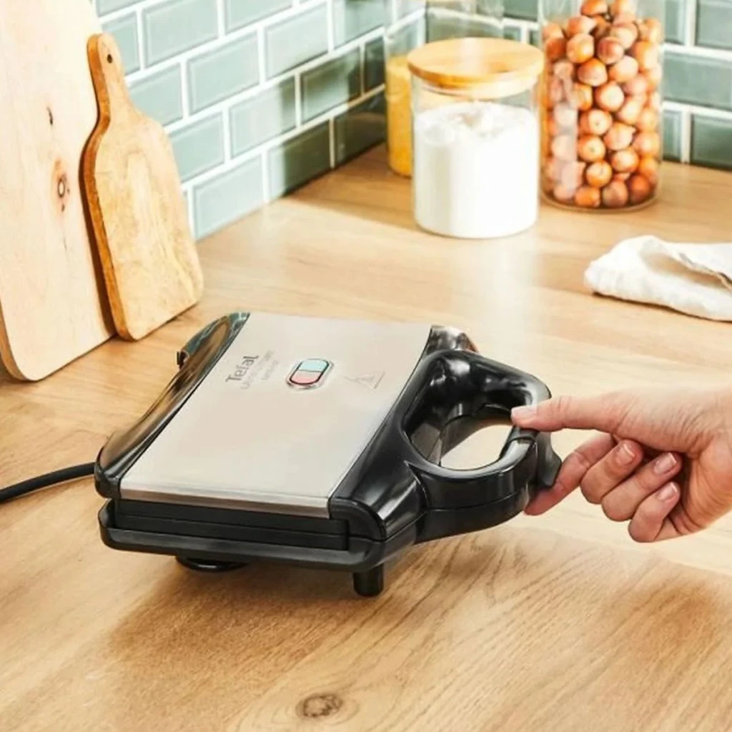 Sandwichera Tefal Ultracompact 700W Negro SM1552, en uso: mano sujetando el asa negro sobre encimera de madera en cocina
