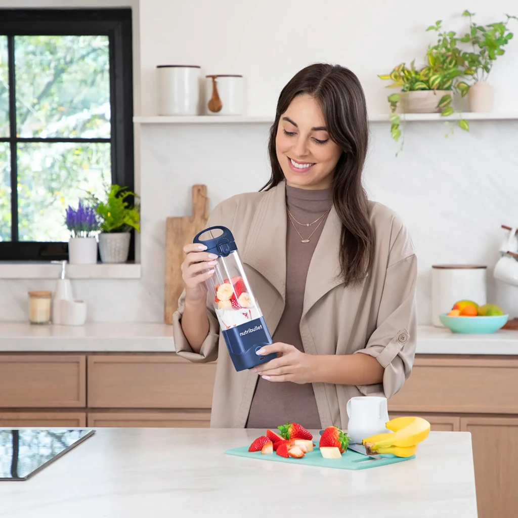 Blender portable NutriBullet 475ml Bleu NBP003NBL, en utilisation: femme en cuisine tient le bol avec des fruits