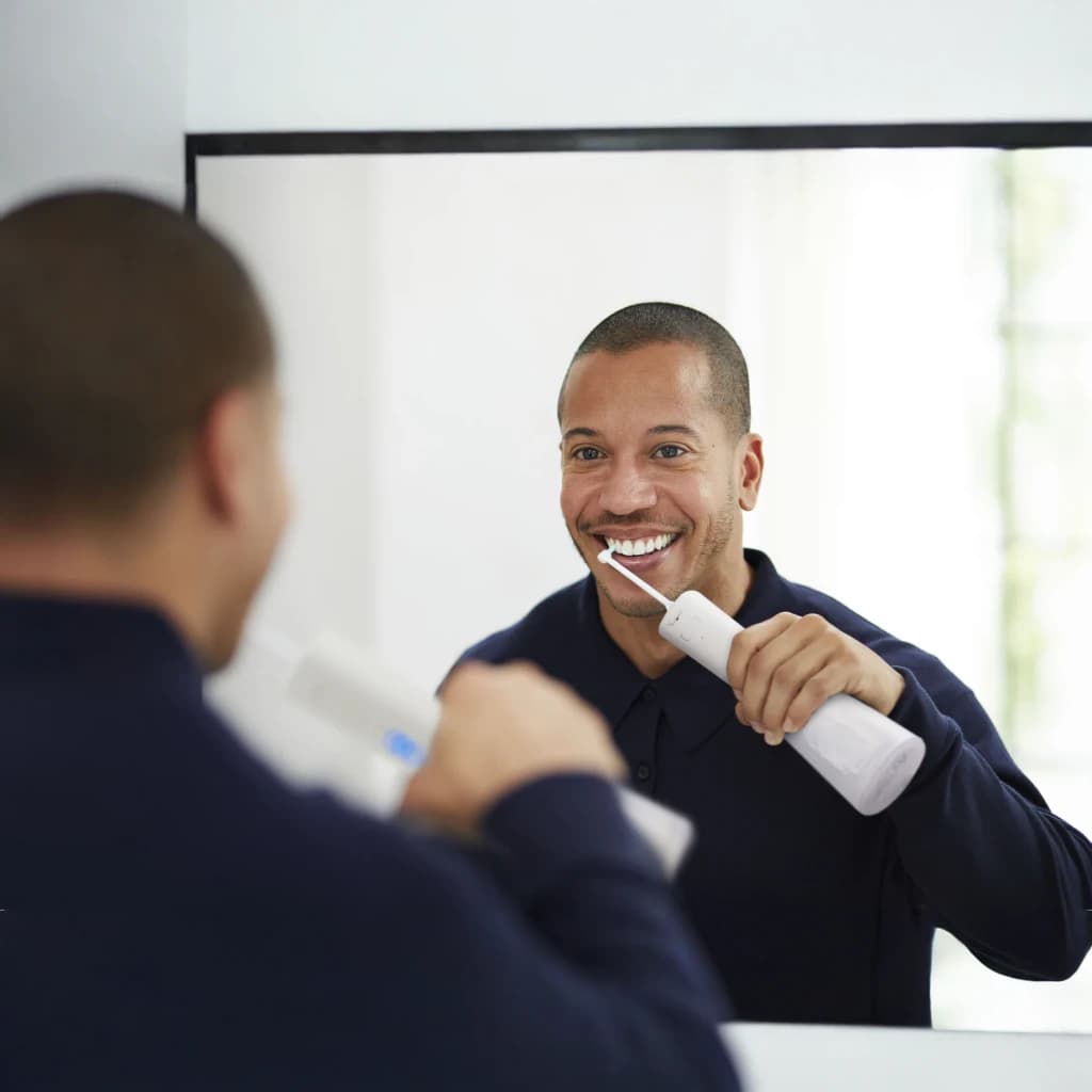 Irrigateur oral Panasonic EW-DJ86 Sans Fil 5 Niveaux Blanc, en utilisation: homme souriant l'utilisant devant le miroir