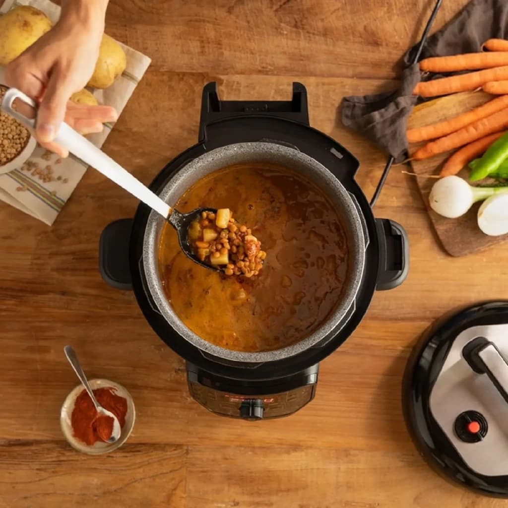 Autocuiseur programmable Cecotec GM H Fry 6L Noir, en utilisation: vue du dessus avec ragoût de lentilles et main remuant à