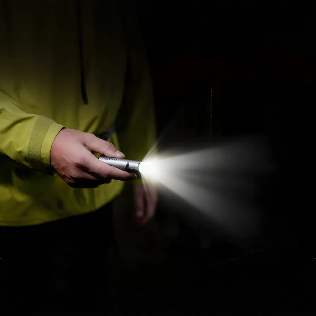 Lanterna LED Flextail Zero 1200 Cinzento USB-C lúmens IP67 até 1 m, em uso: mão com casaco amarelo segura a lanterna acesa