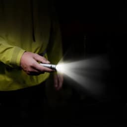 Lanterna LED Flextail Zero 1200 Cinzento USB-C lúmens IP67 até 1 m, em uso: mão com casaco amarelo segura a lanterna acesa