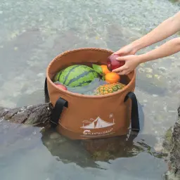 Seau pliable Flextail Flex Bucket 20L Marron 32x25x32cm, en utilisation: fruits rafraîchis en rivière, mains saisissant pomme
