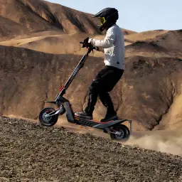 Patinete Eléctrico NAVEE XT5 MAX 700W 110km 25km/h 12 pulgadas, en uso: rider con casco en terreno desértico levantando polvo