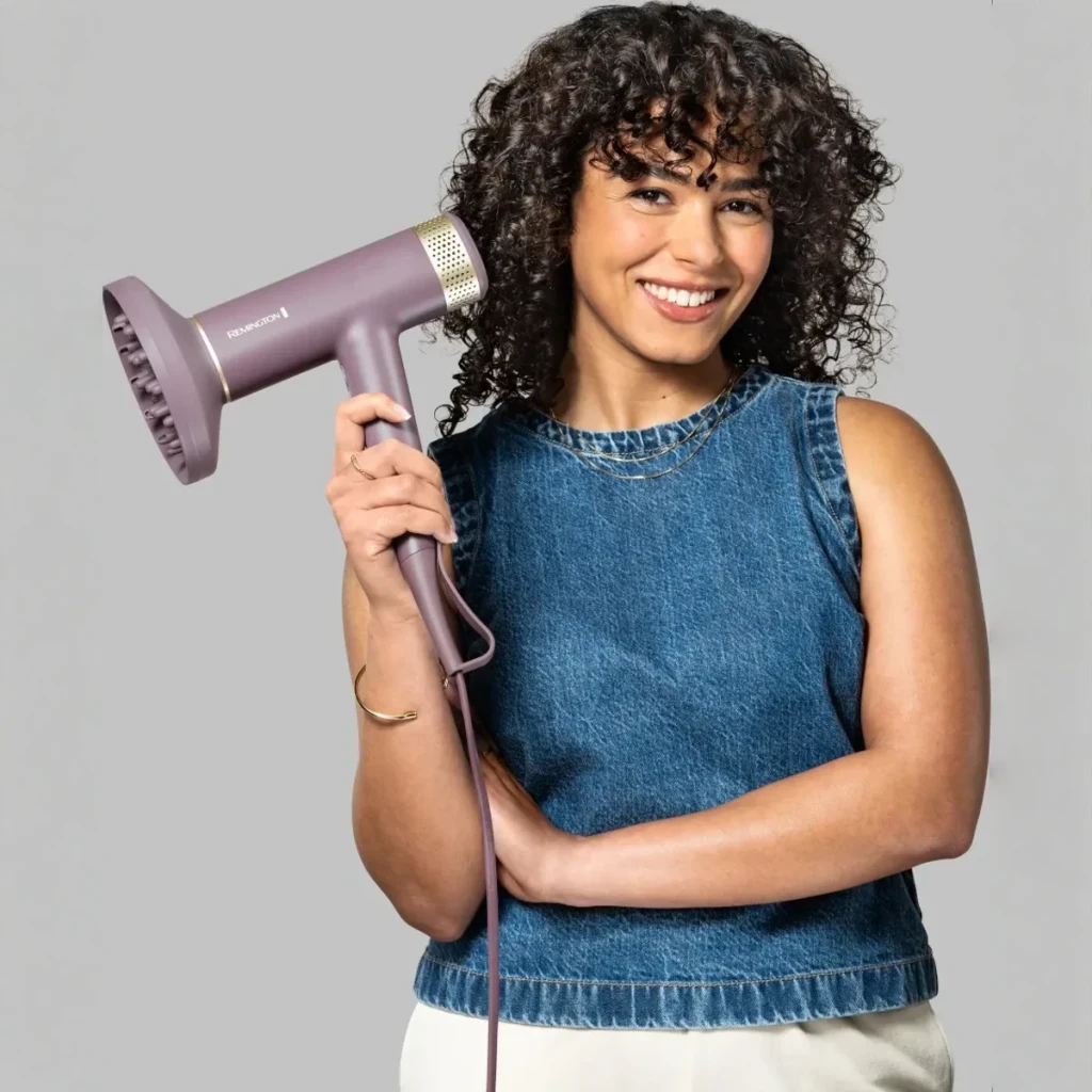 Secador de pelo Remington AIRvive EC8930 Iónico Motor Digital DC 1600W Rosa, en uso: mujer sonriente con cabello rizado