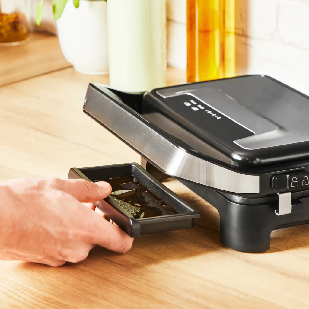 Parrilla eléctrica Moulinex Inicio Compact 1000W 2 personas Negro GI270D, en uso: mano extrayendo bandeja recogegrasas
