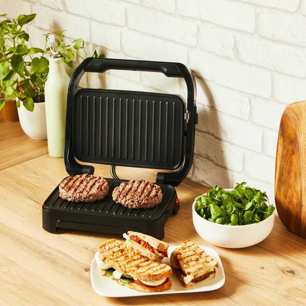 Parrilla eléctrica Moulinex Inicio Compact 1000W 2 personas Negro GI270D, en uso: planchas acanaladas abiertas con 2