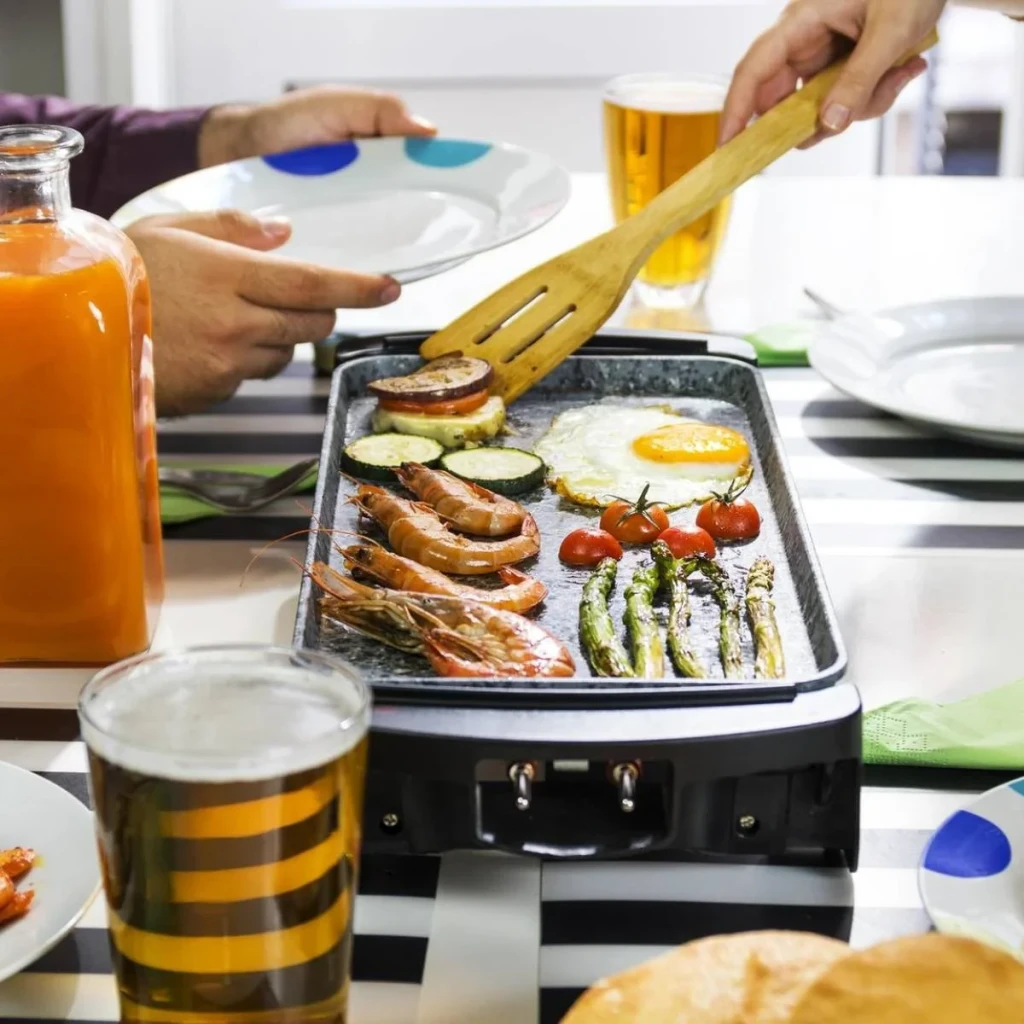 Plancha de asar Cecotec Rock&Water 2000 1800W Negro, en uso: gambas, espárragos, huevo y tomates en la superficie de piedra