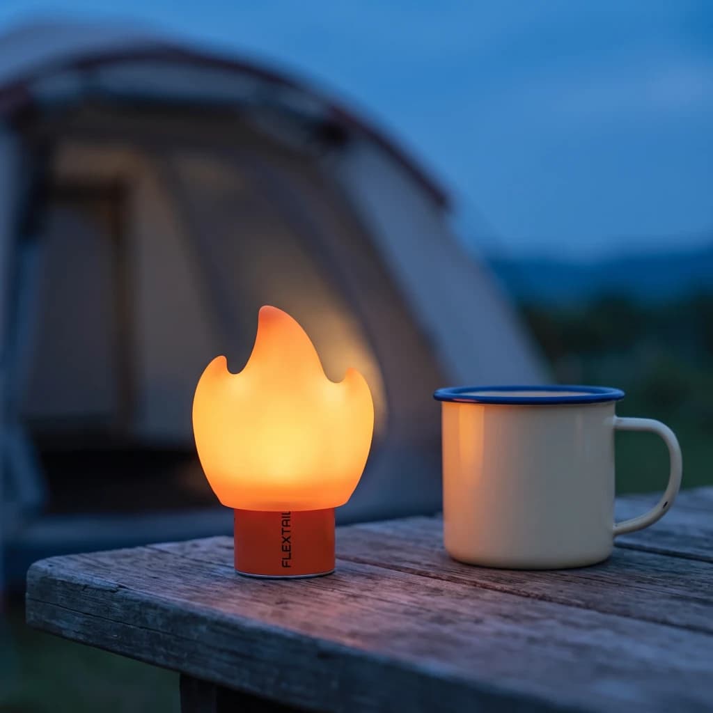 Ecrã difusor Flextail Flame para Tiny Pump 2X Laranja, em uso: aceso sobre mesa de madeira ao anoitecer junto a caneca