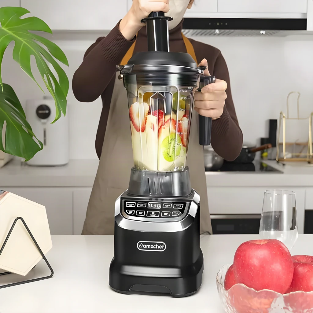 Batidora de vaso AMZCHEF 1,85L 1800W Negro ZM5003-BK, en uso: persona coloca la tapa con frutas y kiwi dentro del vaso