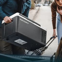 Frigorífico portátil Euhomy CF004 19L 45-60W Preto, em uso: duas pessoas a carregá-lo para o porta-bagagens, pega e grelha