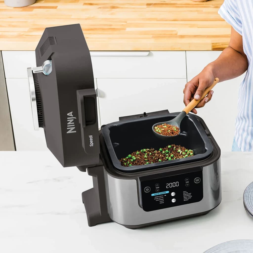 Freidora de Aire Ninja Speedi 5,7L 1760W Negro ON500EU, en uso: tapa abierta con quinoa y guisantes, mano añadiendo