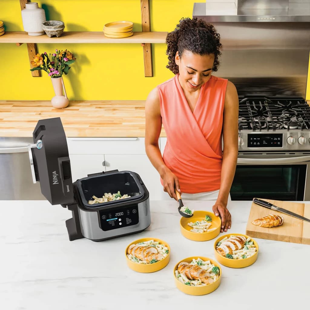 Freidora de Aire Ninja Speedi 5,7L 1760W Negro ON500EU, en uso: mujer sirviendo pasta y pollo en boles amarillos en cocina