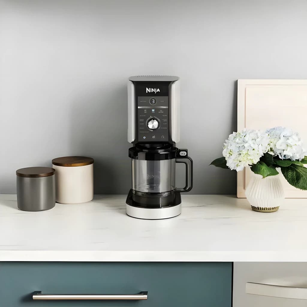 Heladora Ninja CREAMi Deluxe 0,709L 800W Negro NC502EU, vista en cocina: encimera mármol con botes y flores