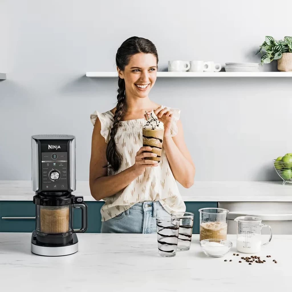 Heladora Ninja CREAMi Deluxe 0,709L 800W Negro NC502EU, en uso: mujer sostiene milkshake con nata junto a la máquina