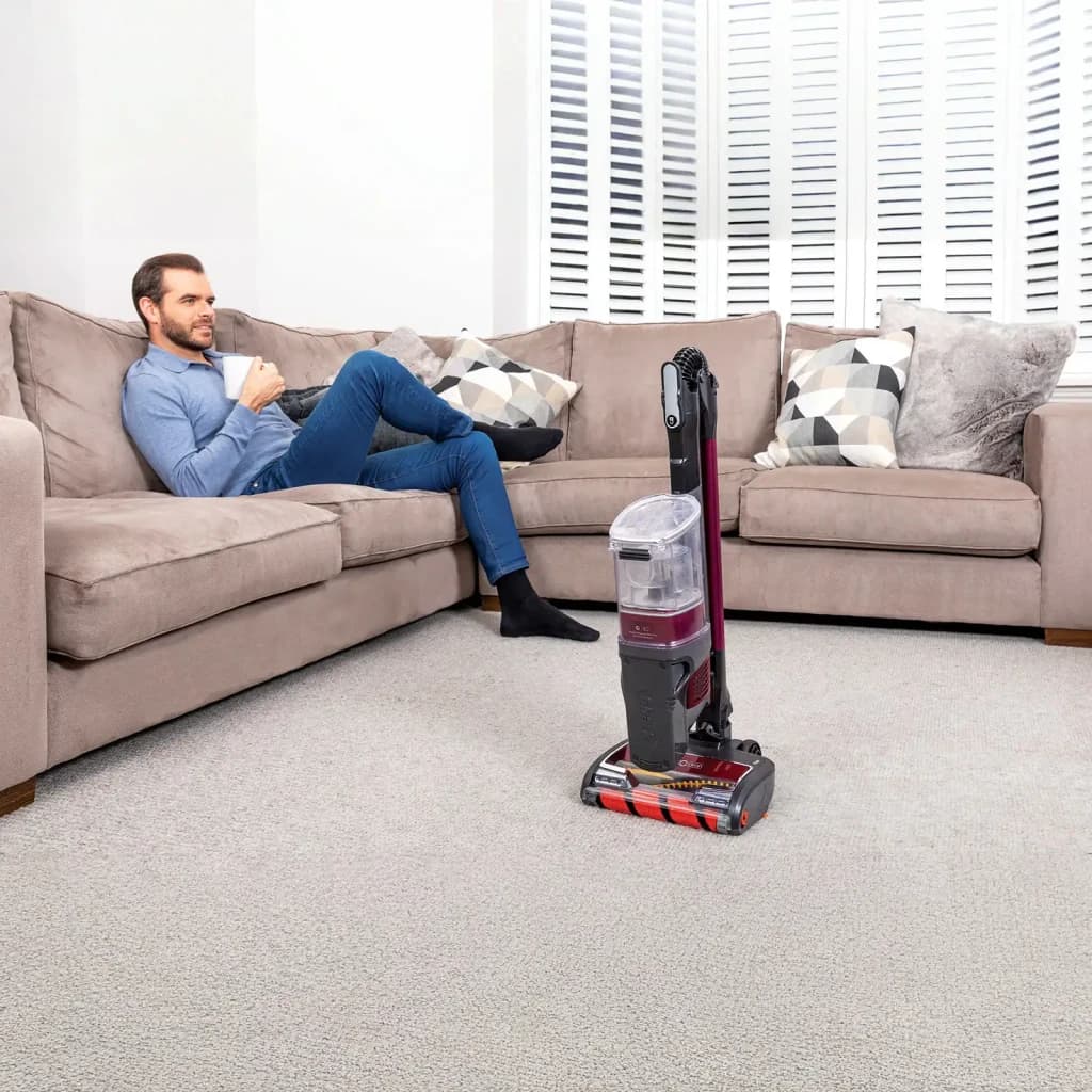 Aspiradora escoba Shark IZ251 2 en 1 Burdeos Sin Cable 45V 80min, en uso: aparcada en salón sobre moqueta, hombre relajado