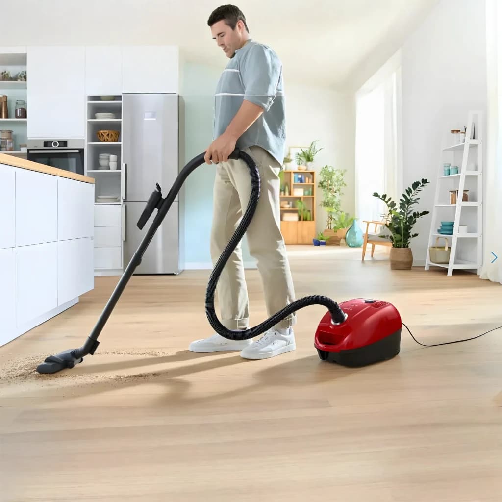 Aspirateur avec sac Bosch Série 4 Rouge 600W BGD38RD1H, en utilisation: homme aspire parquet salon avec flexible et brosse
