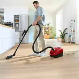 Aspirateur avec sac Bosch Série 4 Rouge 600W BGD38RD1H, en utilisation: homme aspire parquet salon avec flexible et brosse