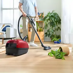 Aspirateur avec sac Bosch Série 4 Rouge 600W BGD38RD1H, en cours d'utilisation: homme aspire parquet avec pot renversé