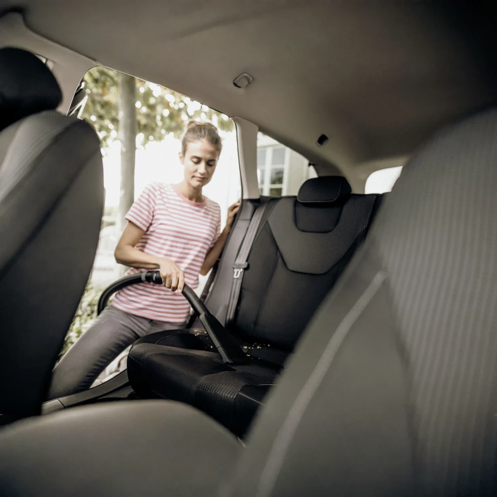 Aspiradora de tambor Kärcher WD 3 S V Amarillo 1000W, en uso: mujer aspirando asientos traseros de coche con boquilla