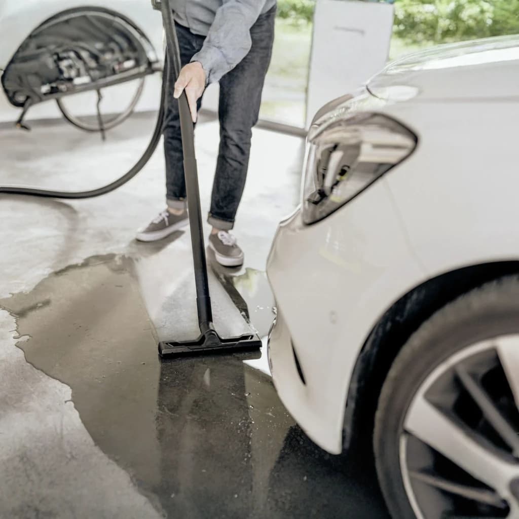Aspiradora de tambor Kärcher WD 3 S V Amarillo 1000W, en uso: boquilla plana aspirando agua del suelo junto a un coche blanco