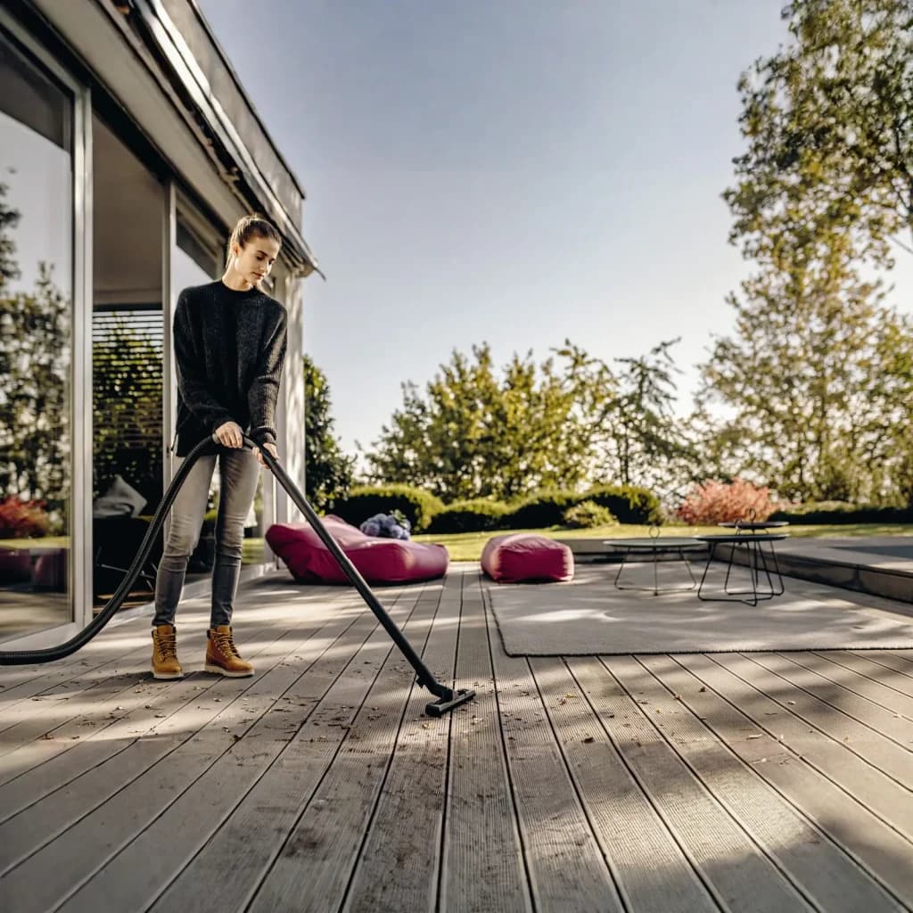 Aspiradora de tambor Kärcher WD 3 S V Amarillo 1000W, en uso: mujer aspirando hojas en terraza de madera exterior