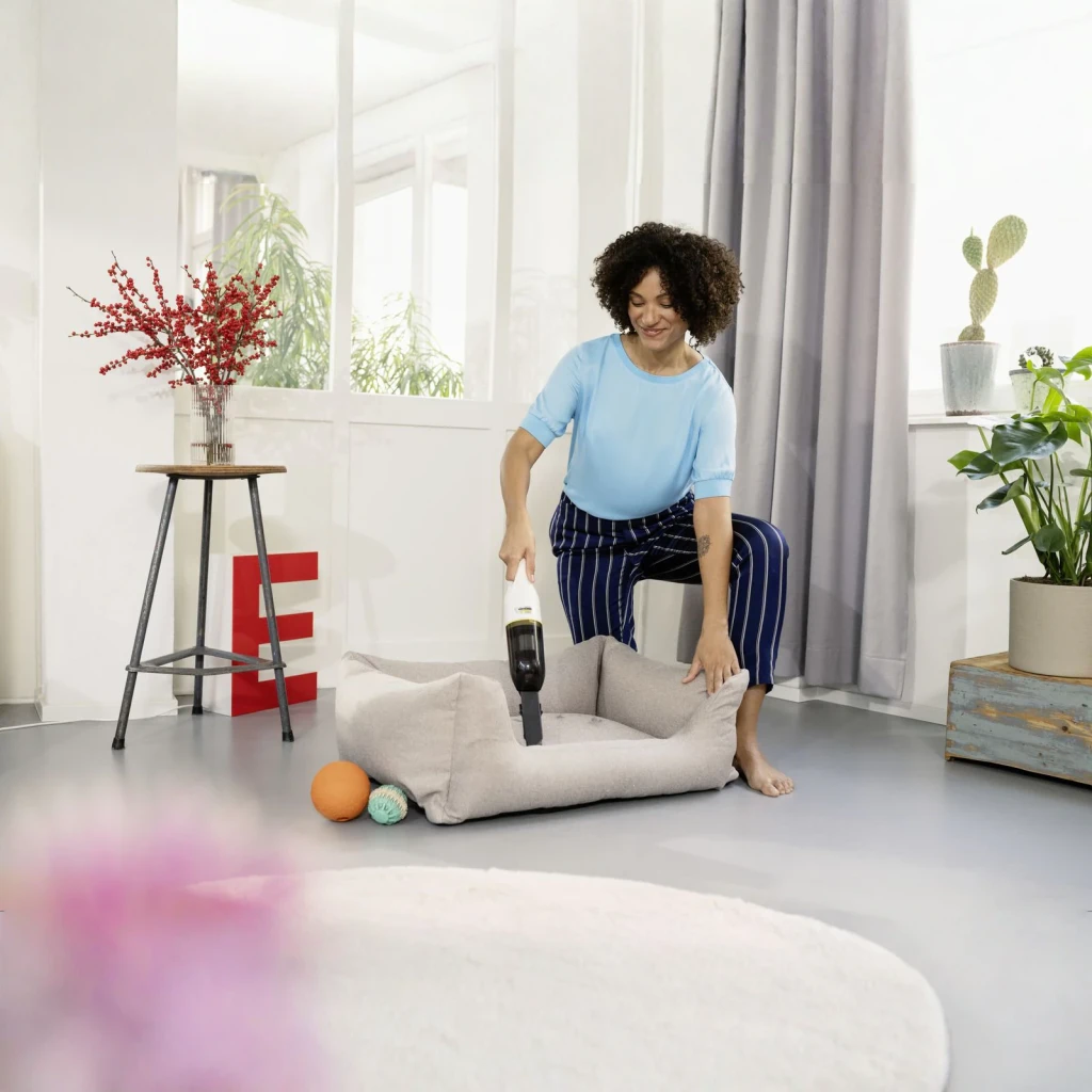 Aspiradora de mano Kärcher CVH 2 Negro/Blanco Sin Cable 7,2V Li-Ion 20min, en uso: mujer aspira cama de mascota en salón