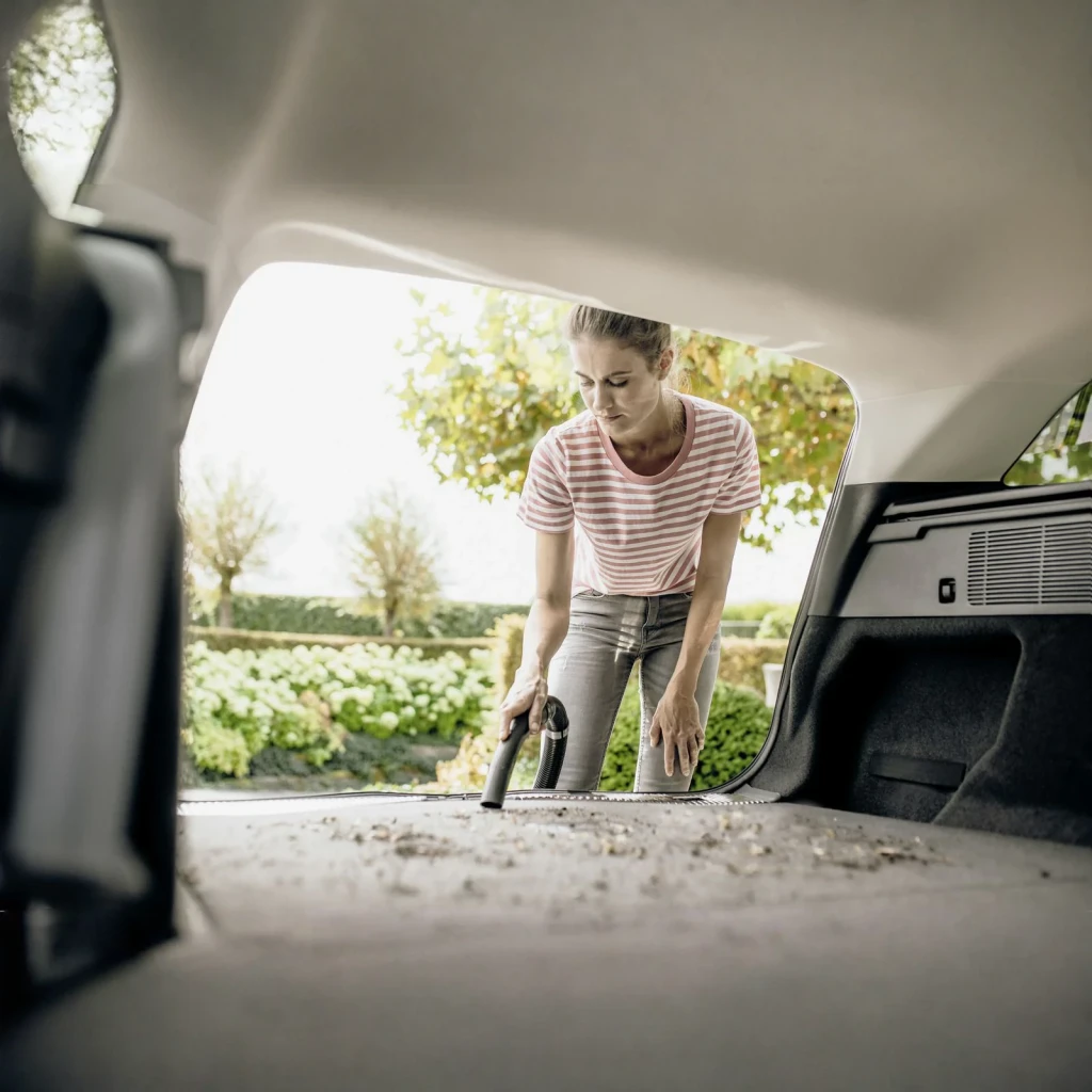 Aspiradora en Seco y Húmedo Kärcher WD 4 Amarillo 1000W V-20/5/22, en uso: mujer aspira el maletero de un coche