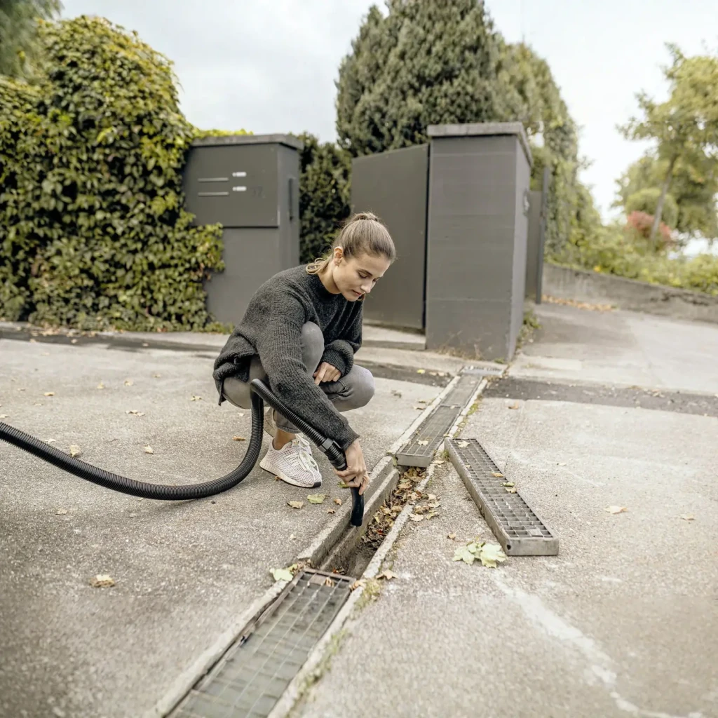 Aspiradora en Seco y Húmedo Kärcher WD 4 Amarillo 1000W V-20/5/22, en uso: mujer aspirando hojas de un desagüe exterior