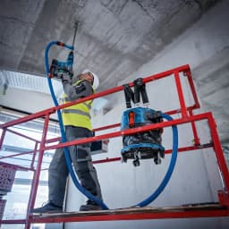 Aspiradora Bosch GAS MC Azul Sin Cable 170mbar 18V-12, en uso: operario en andamio taladra techo conectado a aspiradora azul