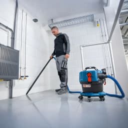 Aspiradora Bosch GAS MC Azul Sin Cable 170mbar 18V-12, en uso: operario aspira suelo de local técnico con manguera azul