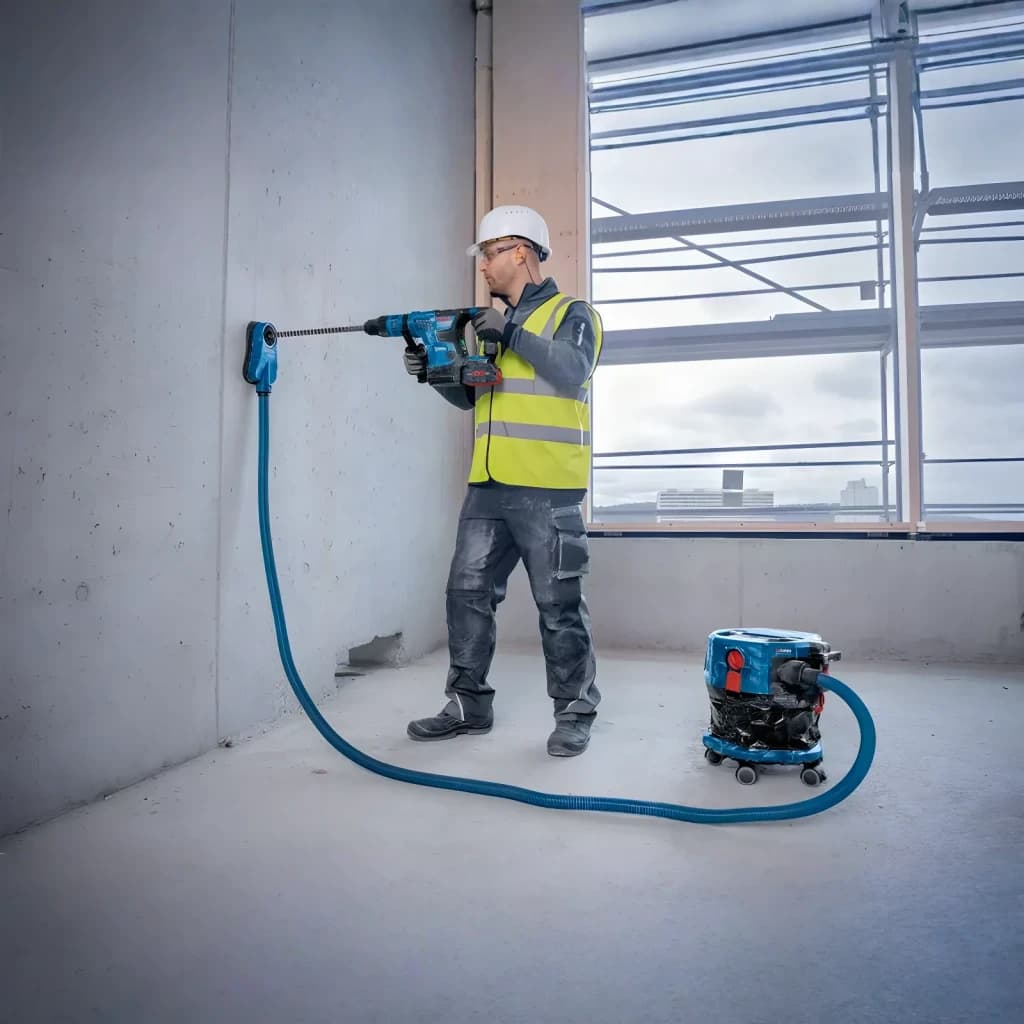 Aspiradora Bosch GAS MC Azul Sin Cable 170mbar 18V-12, en uso: operario taladra pared conectado a aspiradora con manguera