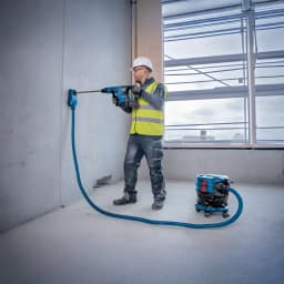 Aspiradora Bosch GAS MC Azul Sin Cable 170mbar 18V-12, en uso: operario taladra pared conectado a aspiradora con manguera