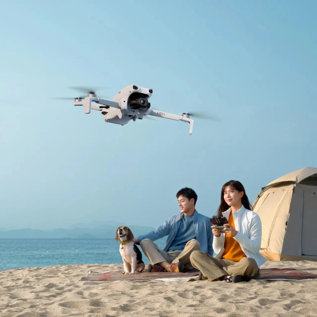 Dron DJI Lito 1 Gris 4K 60fps Gimbal 3 ejes 48MP, en uso: volando sobre pareja con mando en playa con tienda de campaña