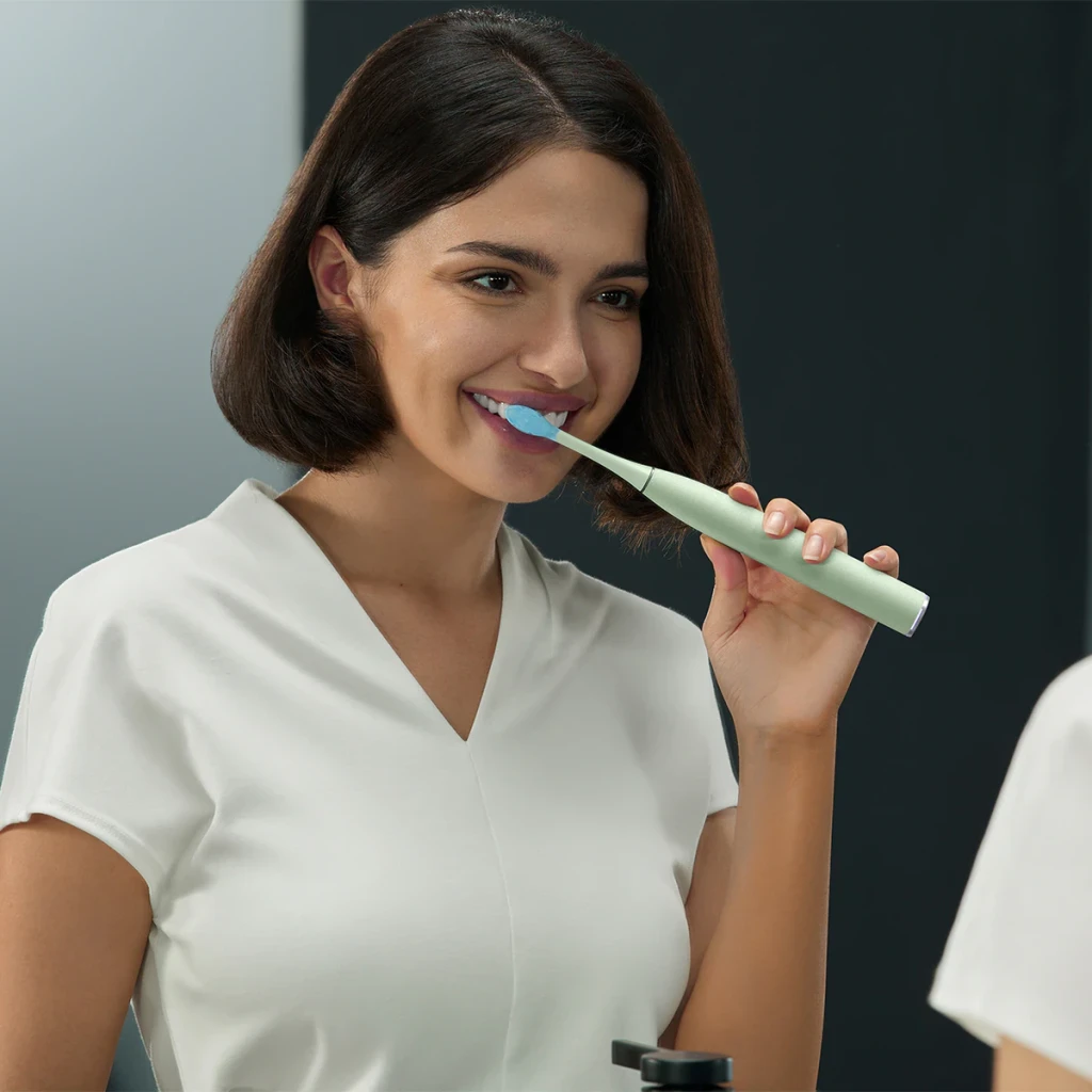 Escova Elétrica Oclean Sónica 84000 mov/min Sem Fios Verde C01000750, uso: mulher sorridente a escovar os dentes em frente