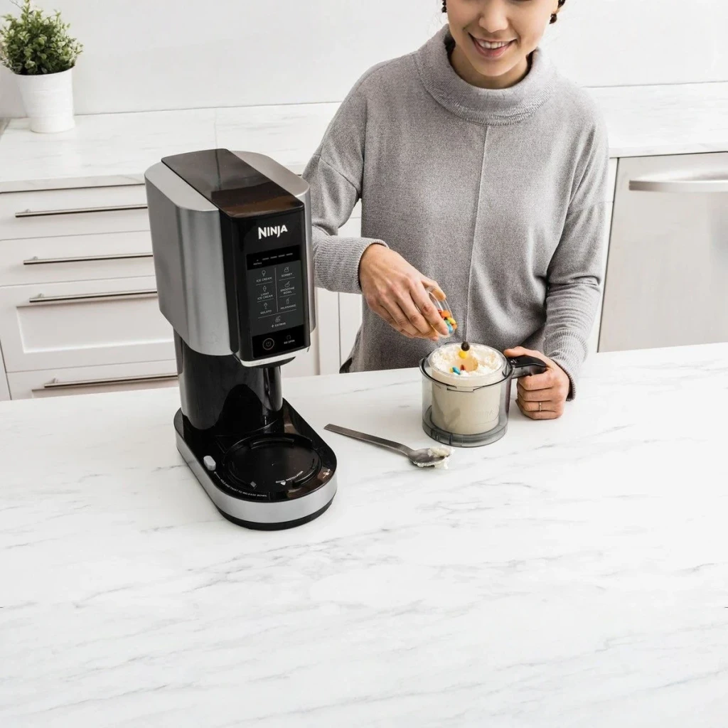 Sorbetière Ninja CREAMi 1,4L 800W Noir/Argent NC300EU, utilisation: personne ajoutant des toppings à la glace dans le bol